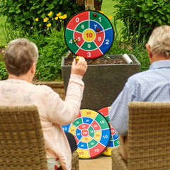 Two people playing with colorful darts on a target outdoors.