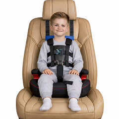 A young boy wearing a gray sweatshirt and sweatpants sits secured in a beige car seat with a black and blue harness. The car seat has black side bolsters with red accents.