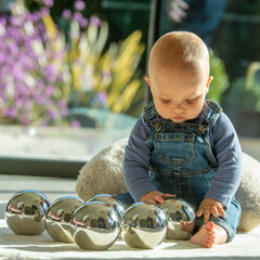 Baby playing with metallic spheres on a surface with a blurred outdoor background