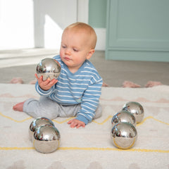 Baby playing with metallic balls on a carpeted floor