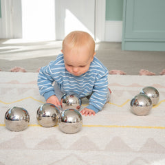 Baby playing with metallic balls on a carpeted floor