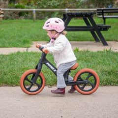 Child riding a balance bike with pink helmet in a park setting