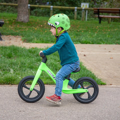 Child riding a green balance bike in a park
