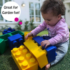 Child playing with large colorful building blocks outdoors.