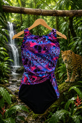 A sleeveless one-piece swimsuit with a vibrant pink, purple, and blue leopard print top and solid black bottoms, hanging on a wooden hanger from a tree branch in a lush jungle setting with a waterfall and a leopard in the background. AI