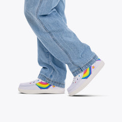 White sneakers with rainbow designs worn with light blue jeans on a white background