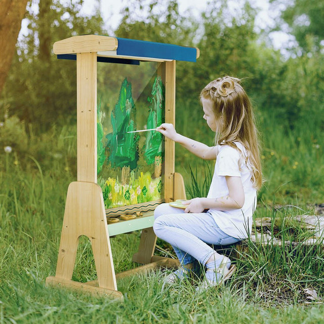 Child painting on an outdoor easel in a grassy area