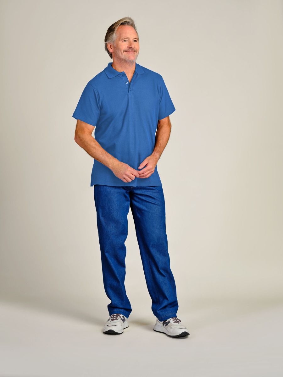 A man wearing a blue short-sleeve polo shirt and matching blue pants, standing against a plain light beige studio background.