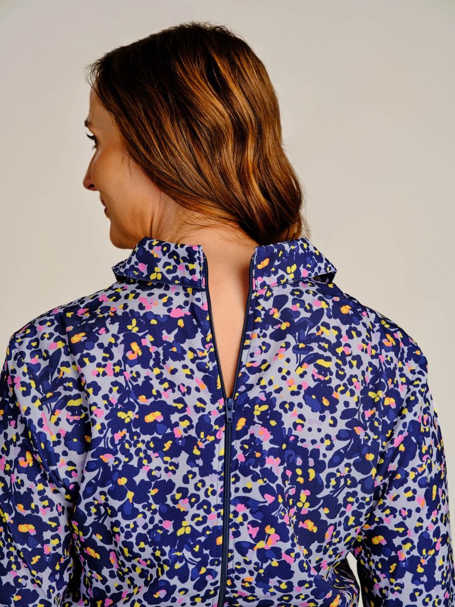 A woman shown from the back wearing a long-sleeve high-neck jacket with a colorful abstract floral pattern in purple, blue, pink, yellow, and white.