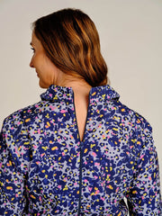 A woman shown from the back wearing a long-sleeve high-neck jacket with a colorful abstract floral pattern in purple, blue, pink, yellow, and white.