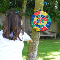Person playing with a colorful outdoor dartboard in a garden setting.