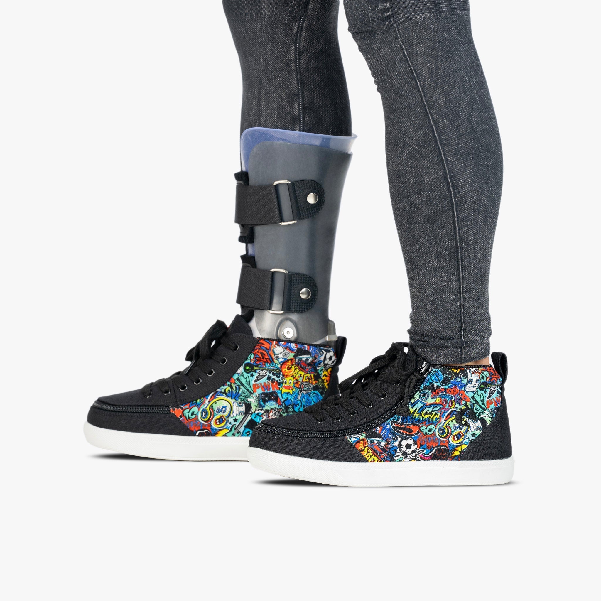 A person wearing a gray lower-leg cast attached to black high-top sneakers with colorful graffiti-style panels, standing against a light gray studio background.