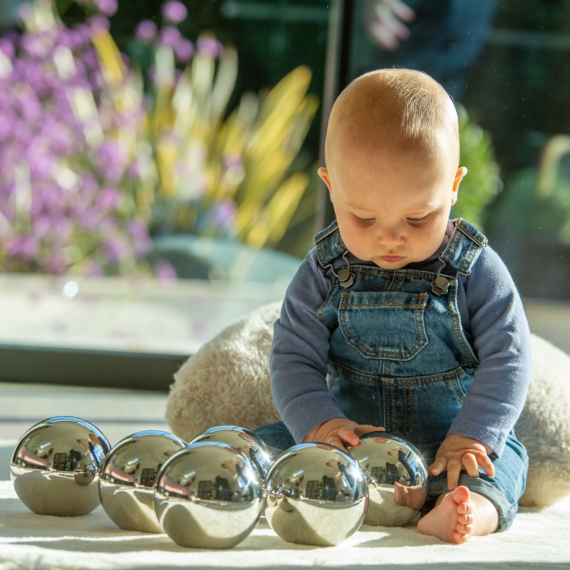 Baby playing with metallic spheres on a surface with a blurred outdoor background