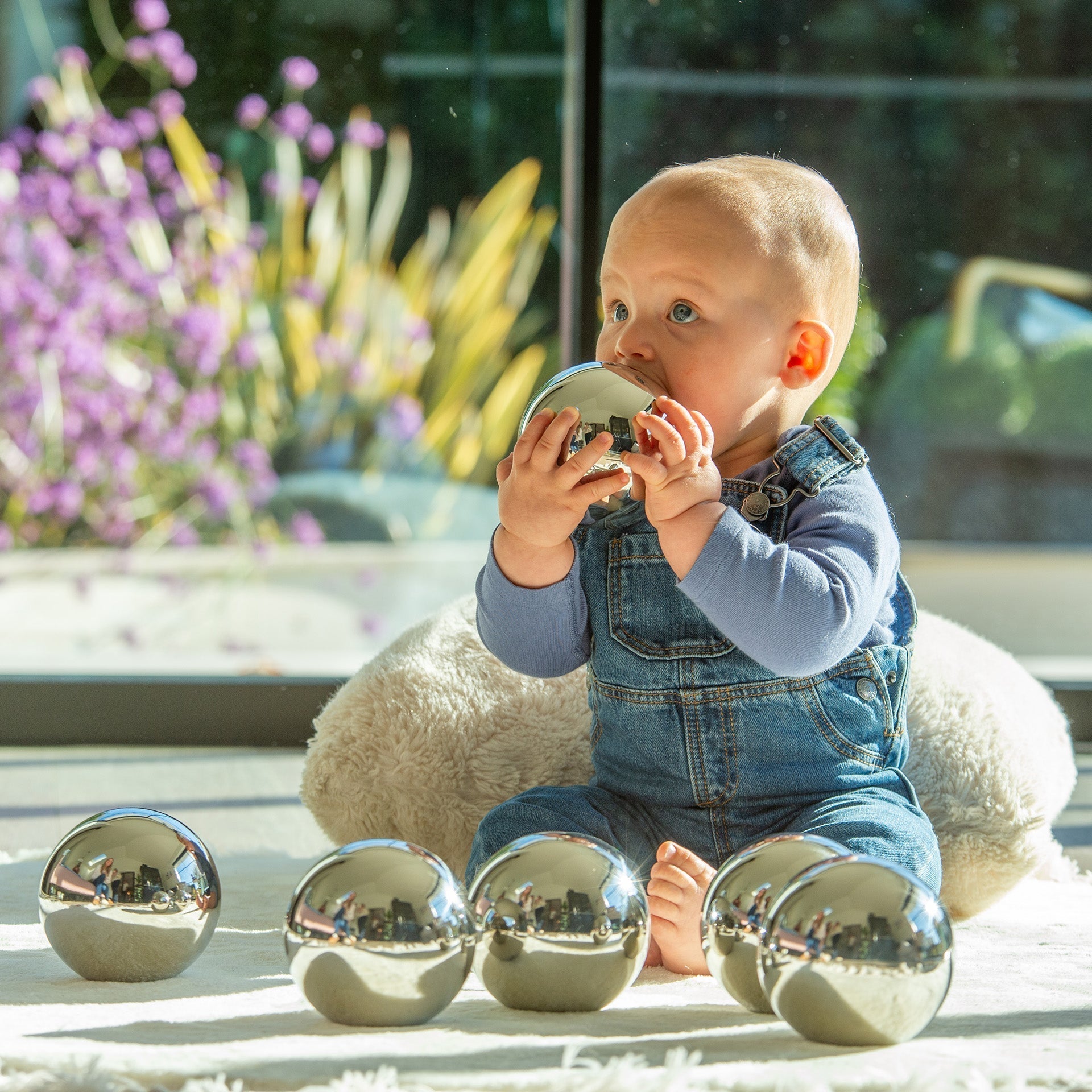 Baby playing with metallic balls on a light surface with flowers in the background