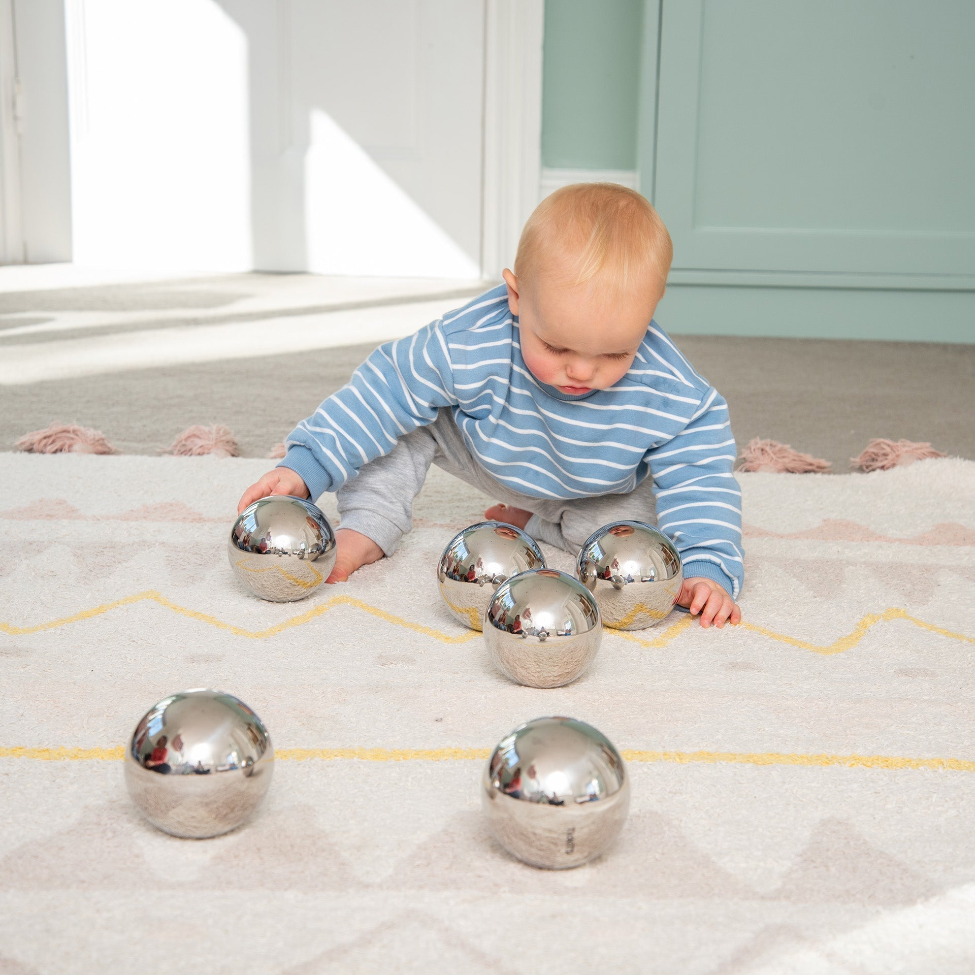 Baby playing with shiny metallic balls on a patterned rug.