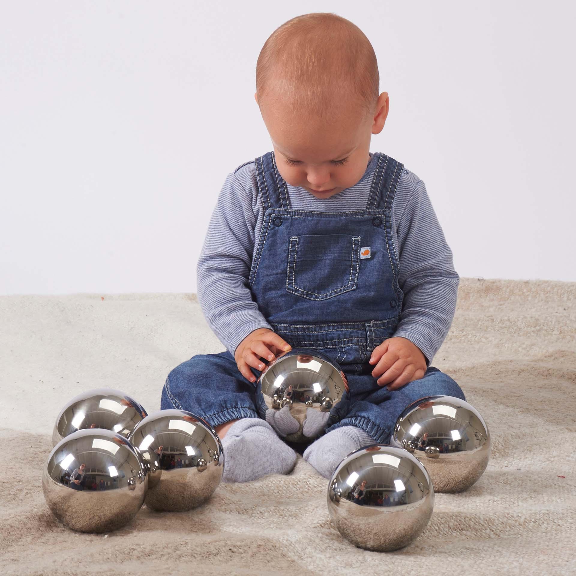 Baby playing with metallic balls on a neutral background
