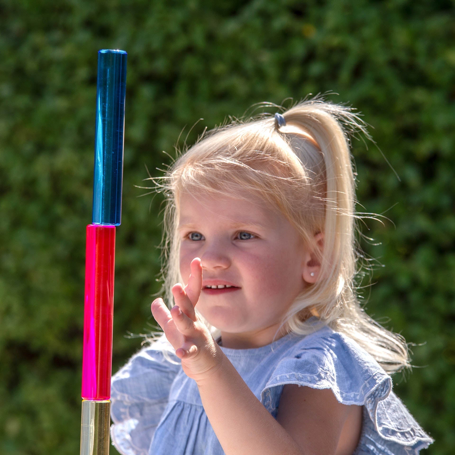 Young girl holding a colorful stick with a blue top and pink bottom against a green background