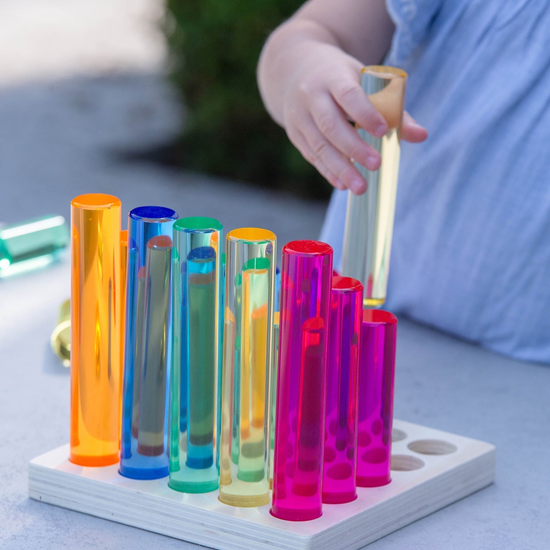 Colorful test tube-like objects on a wooden base with a child's hand interacting with them.