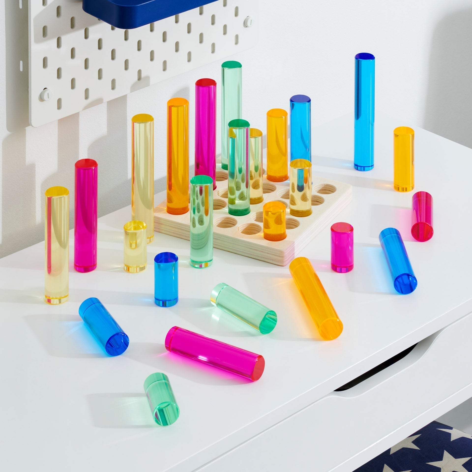 Colorful plastic tubes on a white surface with a pegboard in the background