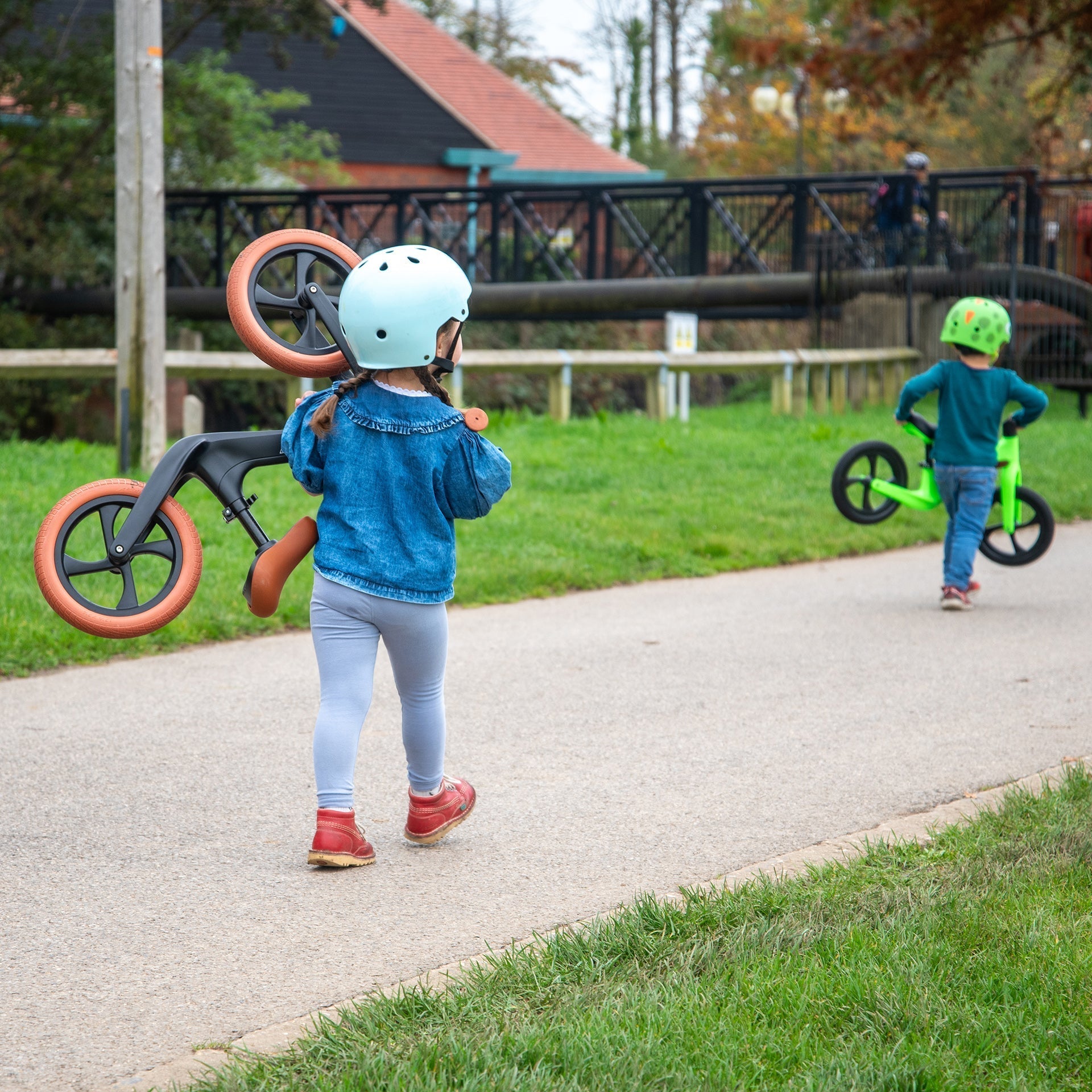 Two children with balance bikes on a paved path in a park.