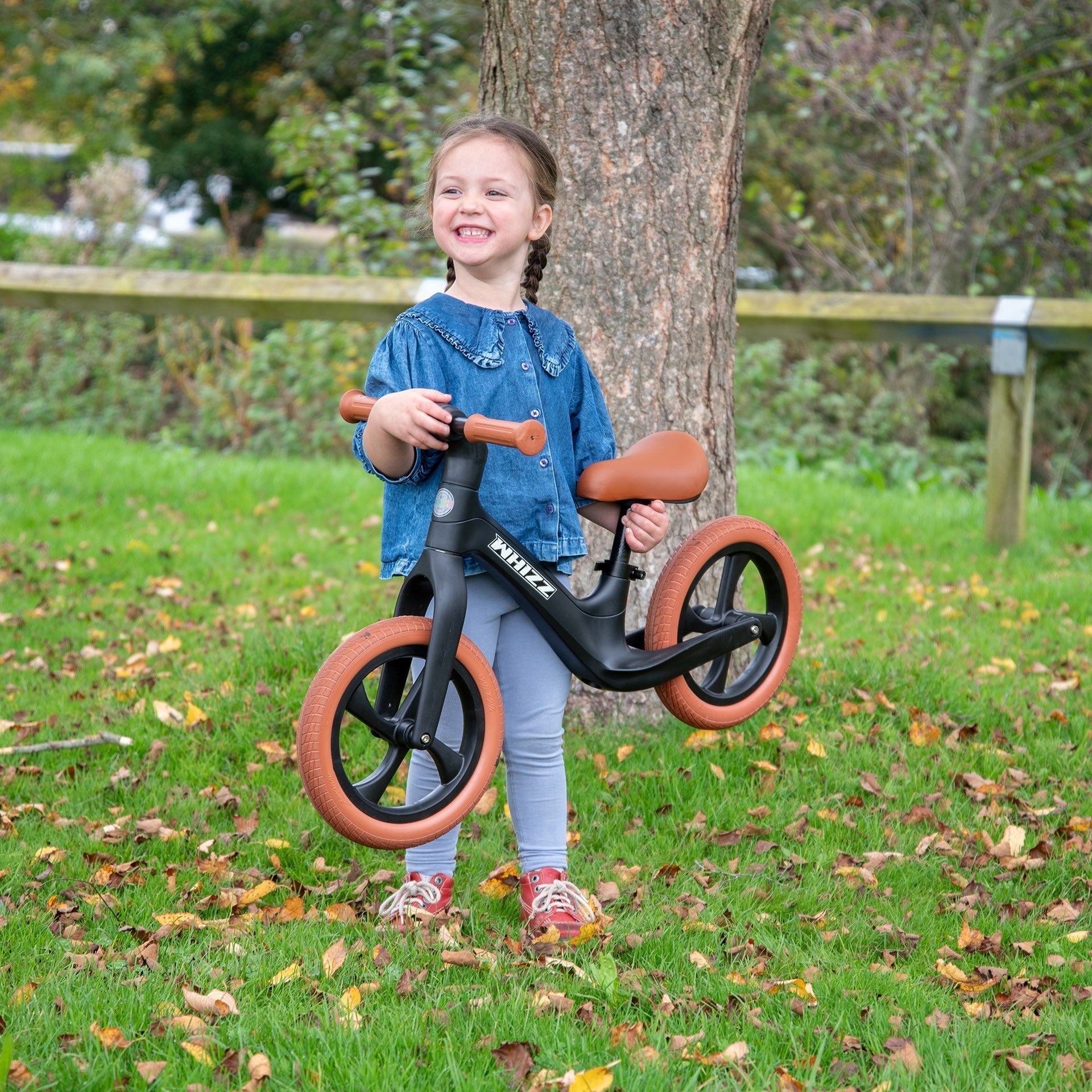 Child holding a balance bike in a park setting