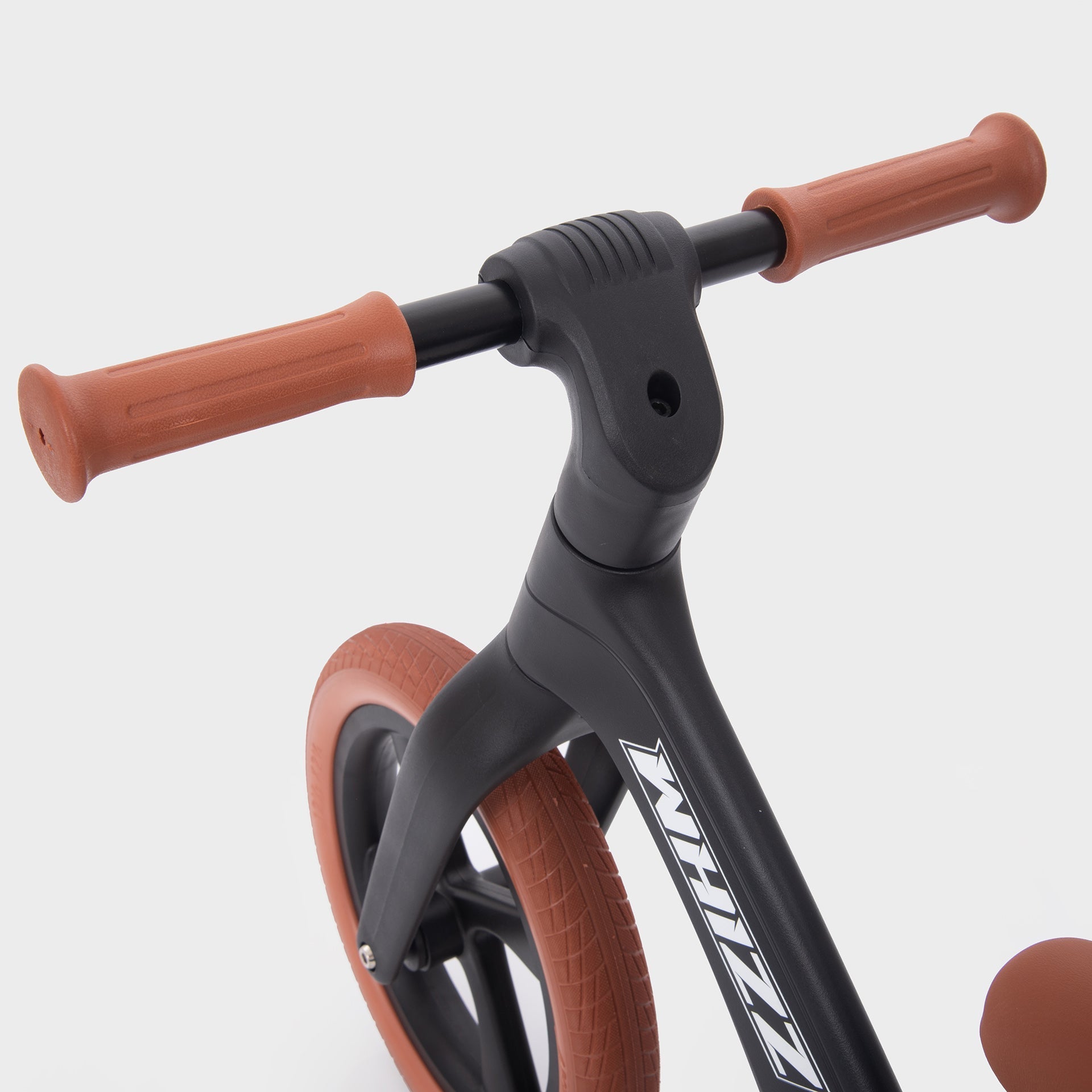 Close-up of a balance bike with brown handlebar grips and wheels on a white background