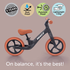 Black balance bike with orange wheels on a brown background, featuring certification icons and text.