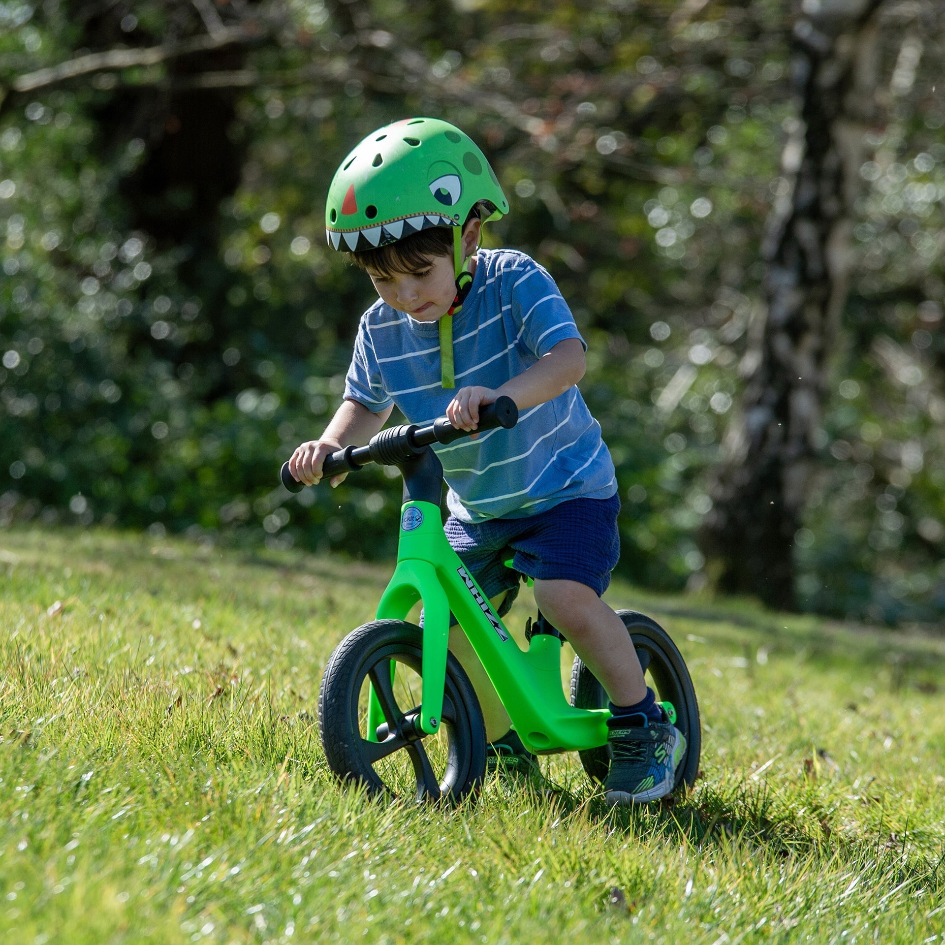 Child riding a green balance bike outdoors with a helmet.