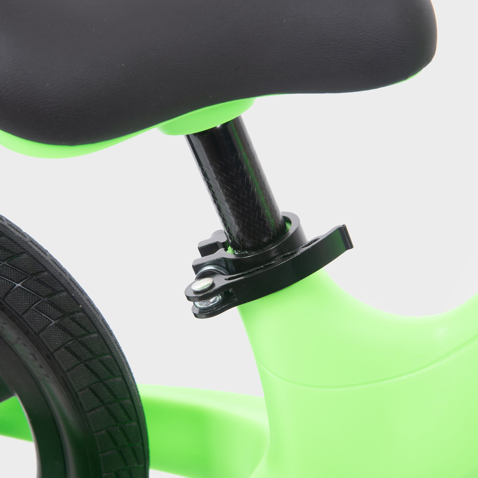 Close-up of a green balance bike with black seat and wheel on a light gray background
