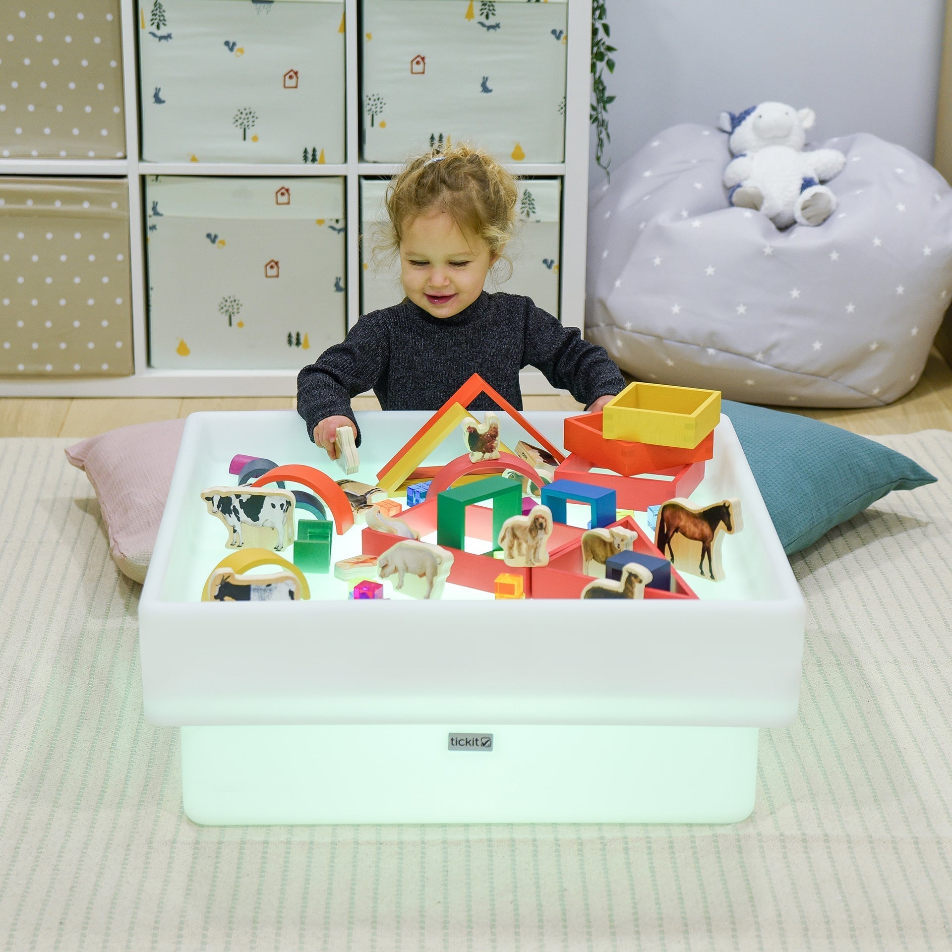 Child playing with a colorful toy set on a light-up table in a child's room.