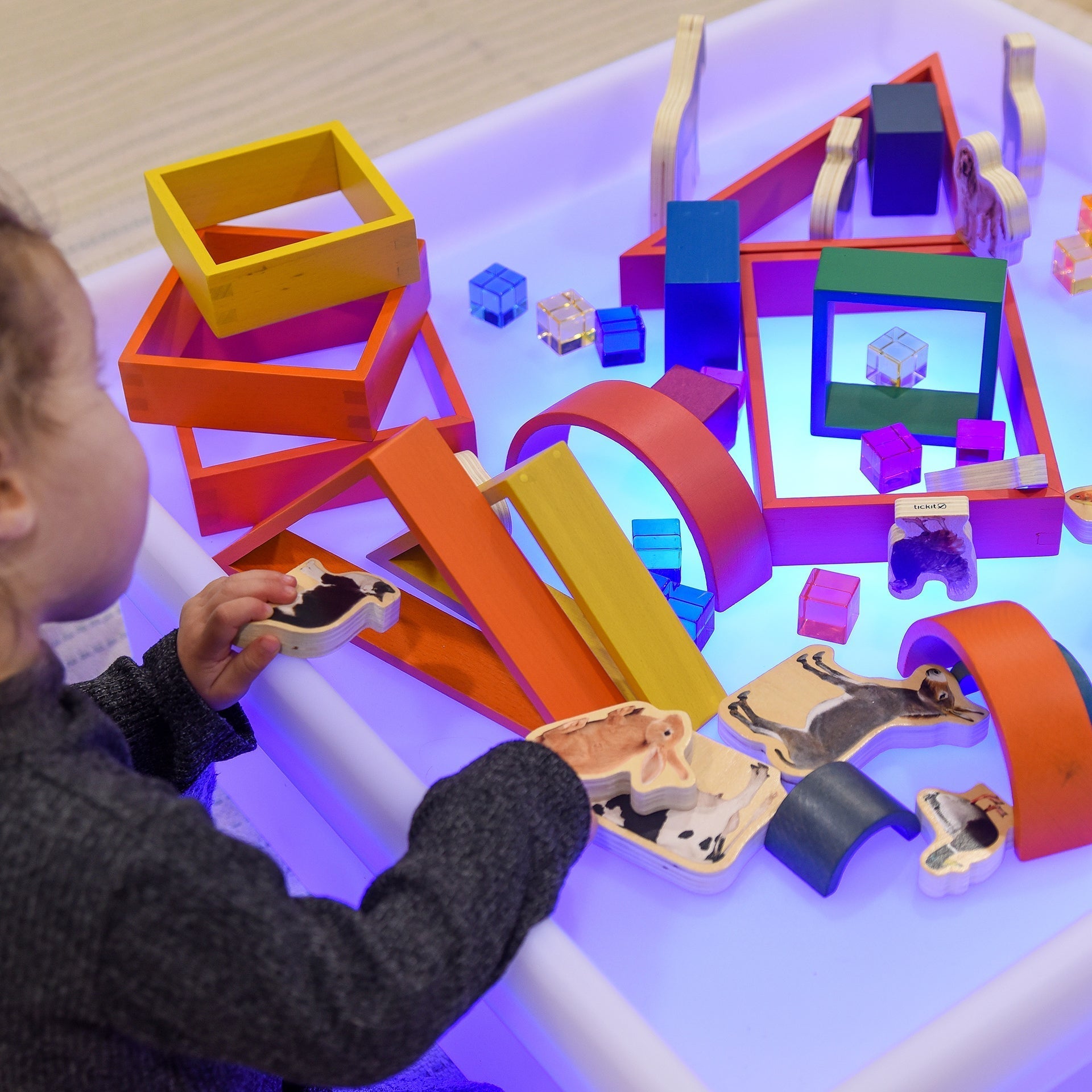 Child playing with colorful geometric shapes on a light-up table