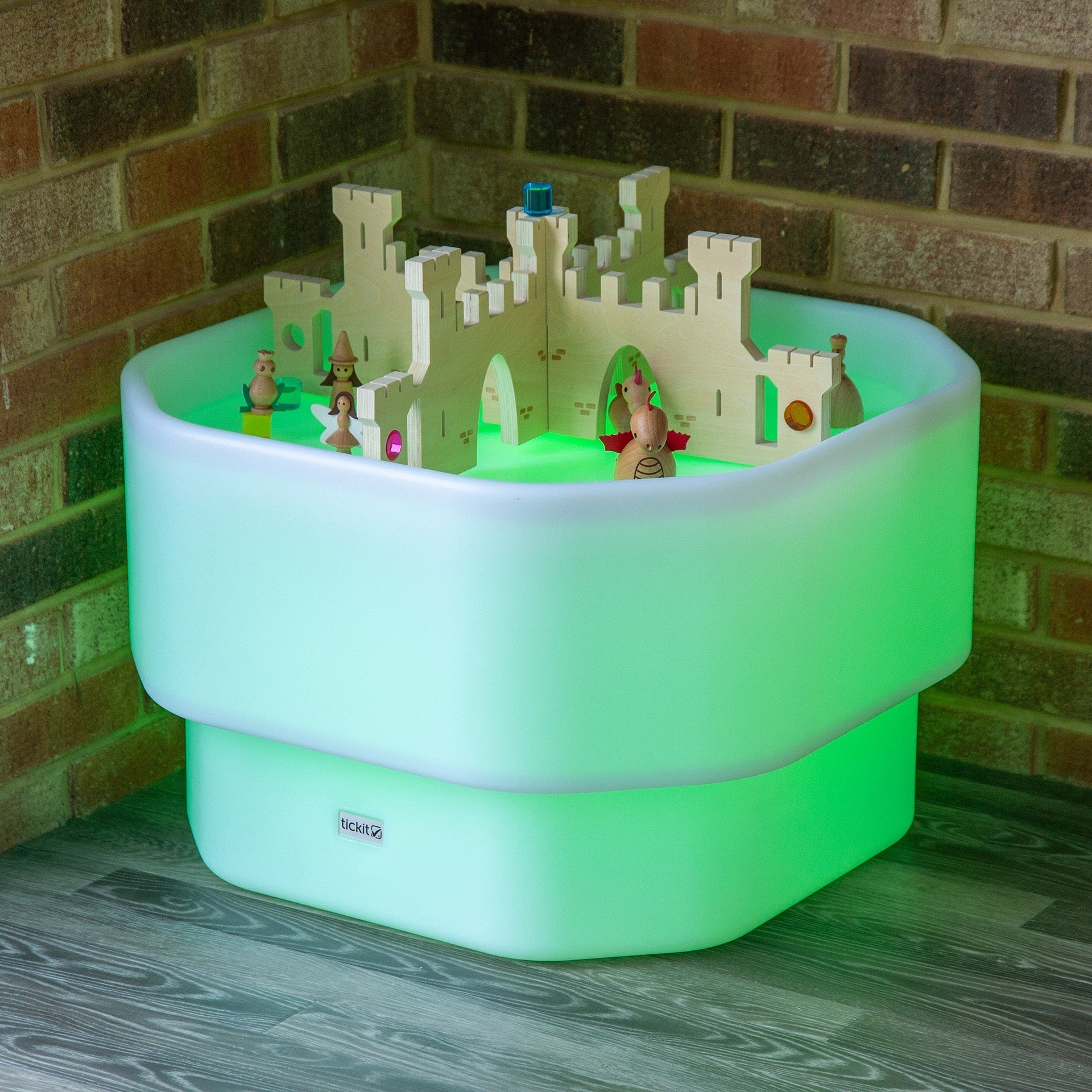 Toy castle on a glowing green platform against a brick wall.