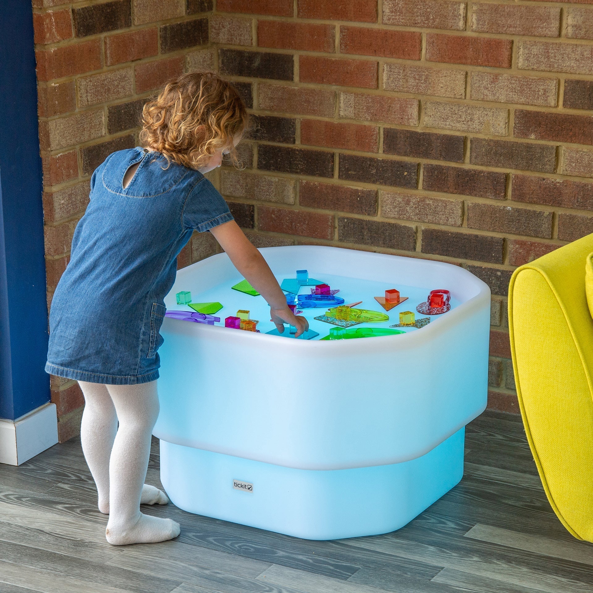 Child playing with colorful toys in a light blue play table against a brick wall.
