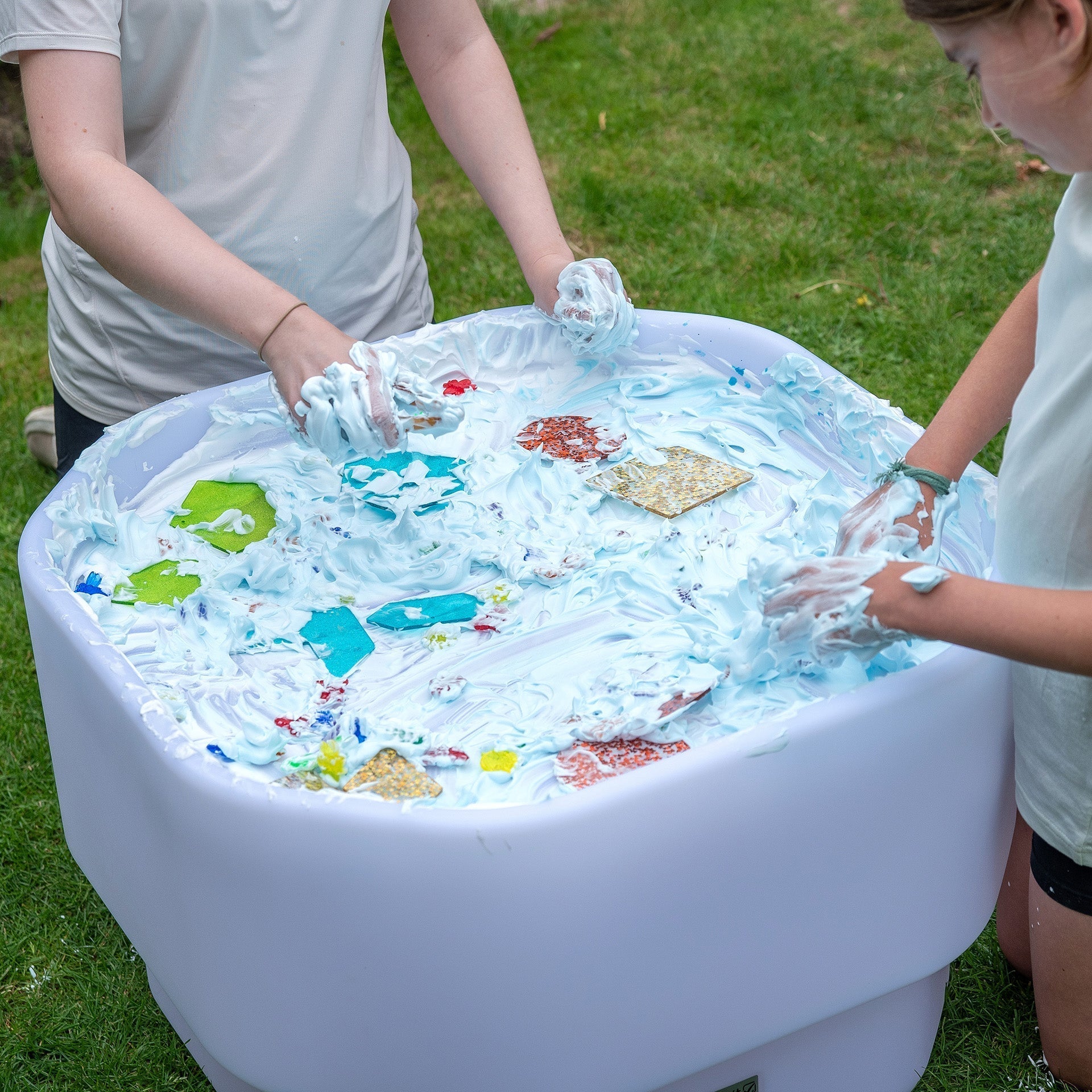 Two people playing with a sensory play table outdoors on grass