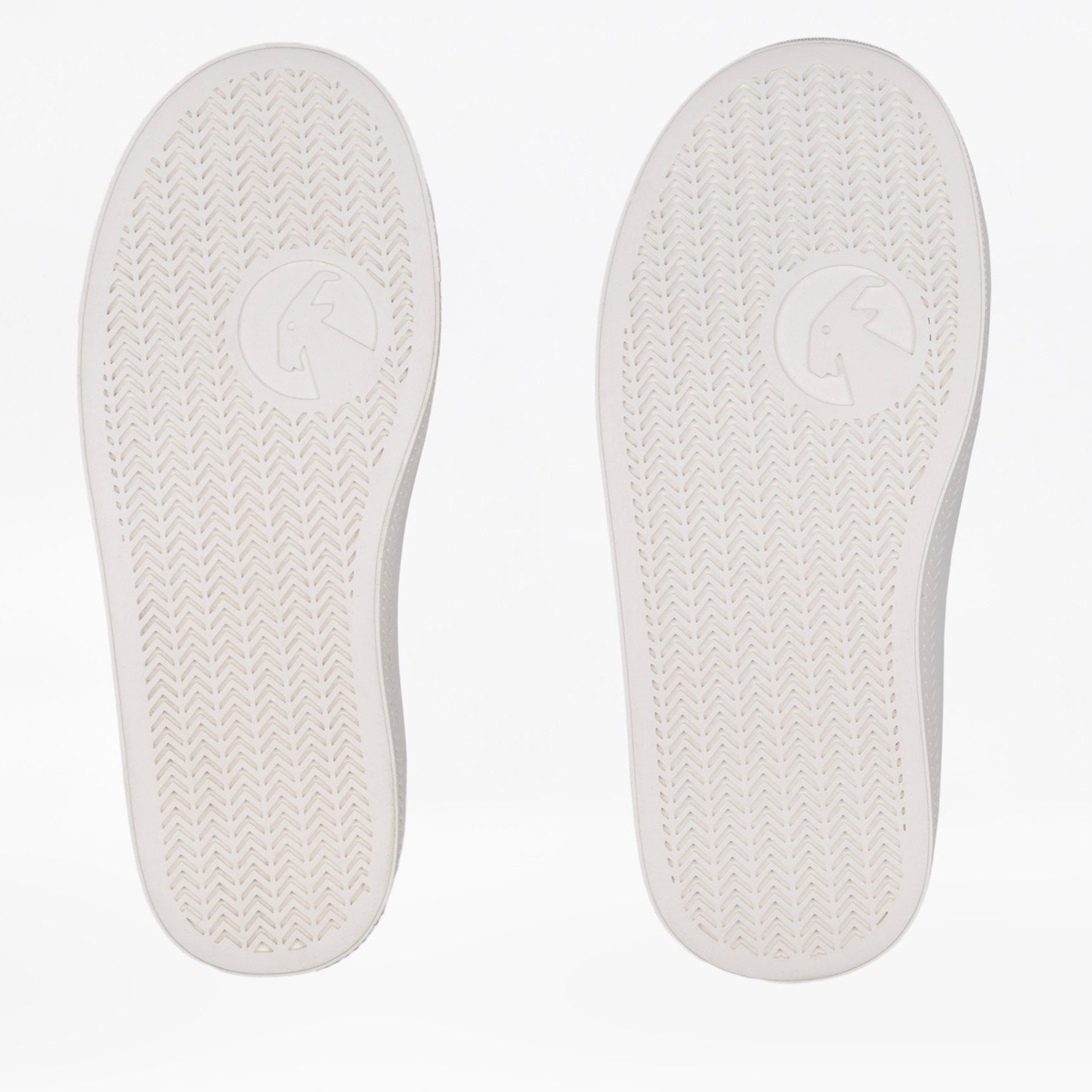 A pair of white slip-on shoes shown from the bottom, featuring a textured herringbone pattern and a circular horse logo in the center of each sole.