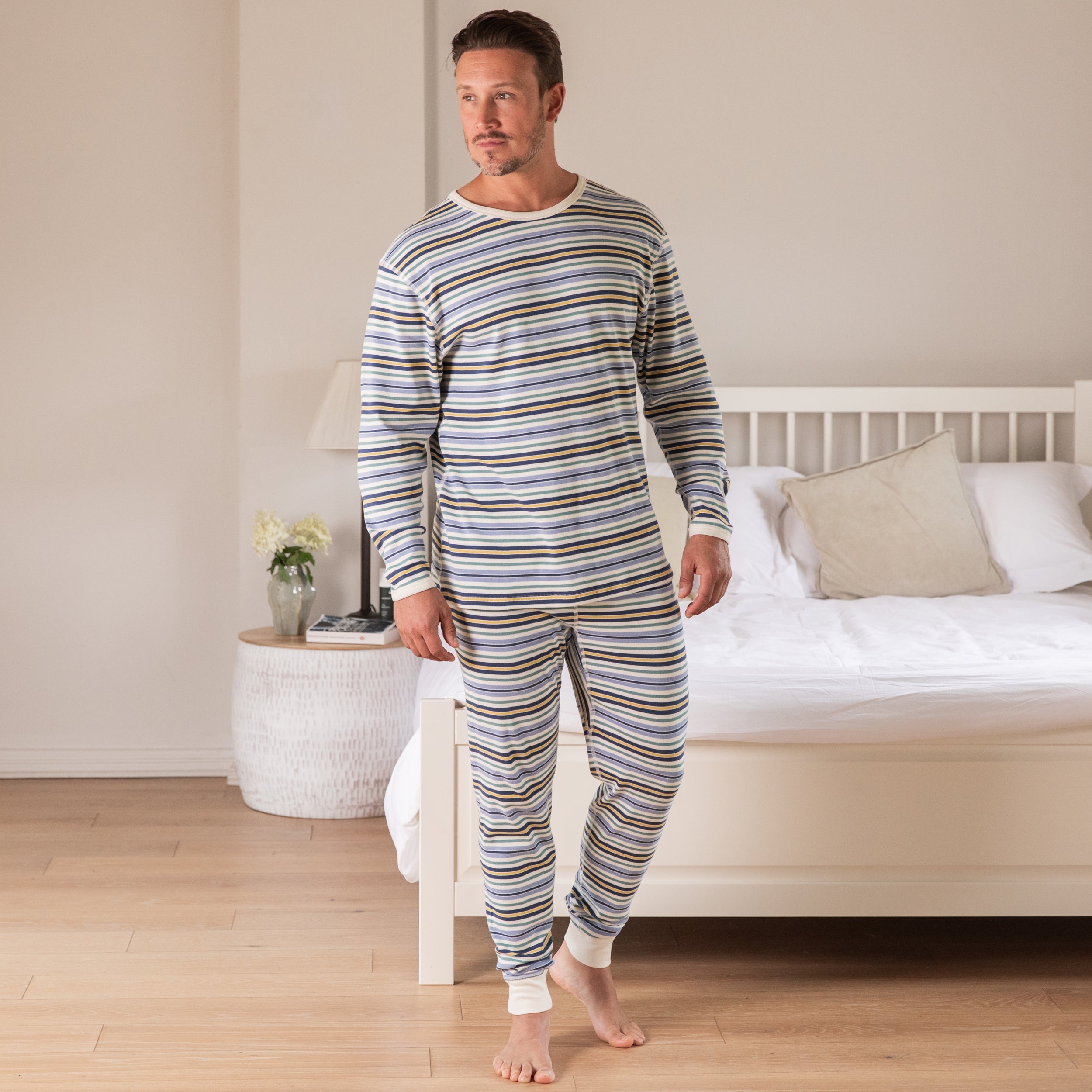 Man wearing striped pajamas standing in a bedroom.