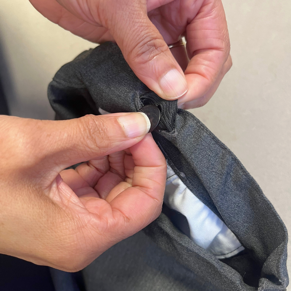 Person sewing a button onto a piece of gray fabric.