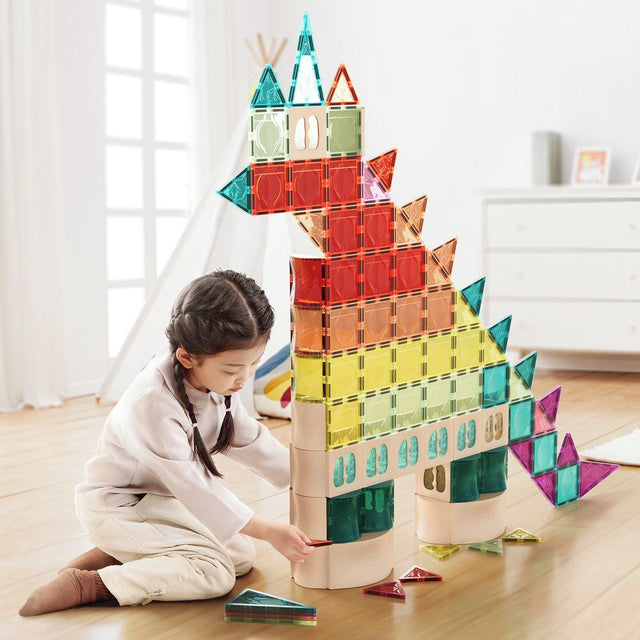Child playing with colorful magnetic building blocks on a wooden floor.