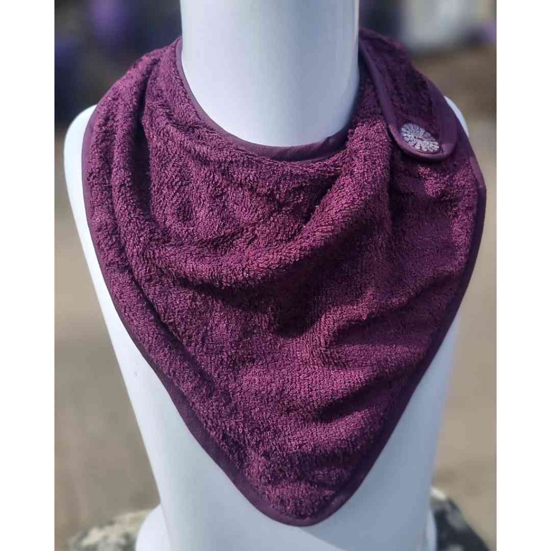 A deep purple textured bandana bib or neck warmer displayed on a white mannequin bust, featuring a snap-button strap closure on the side.