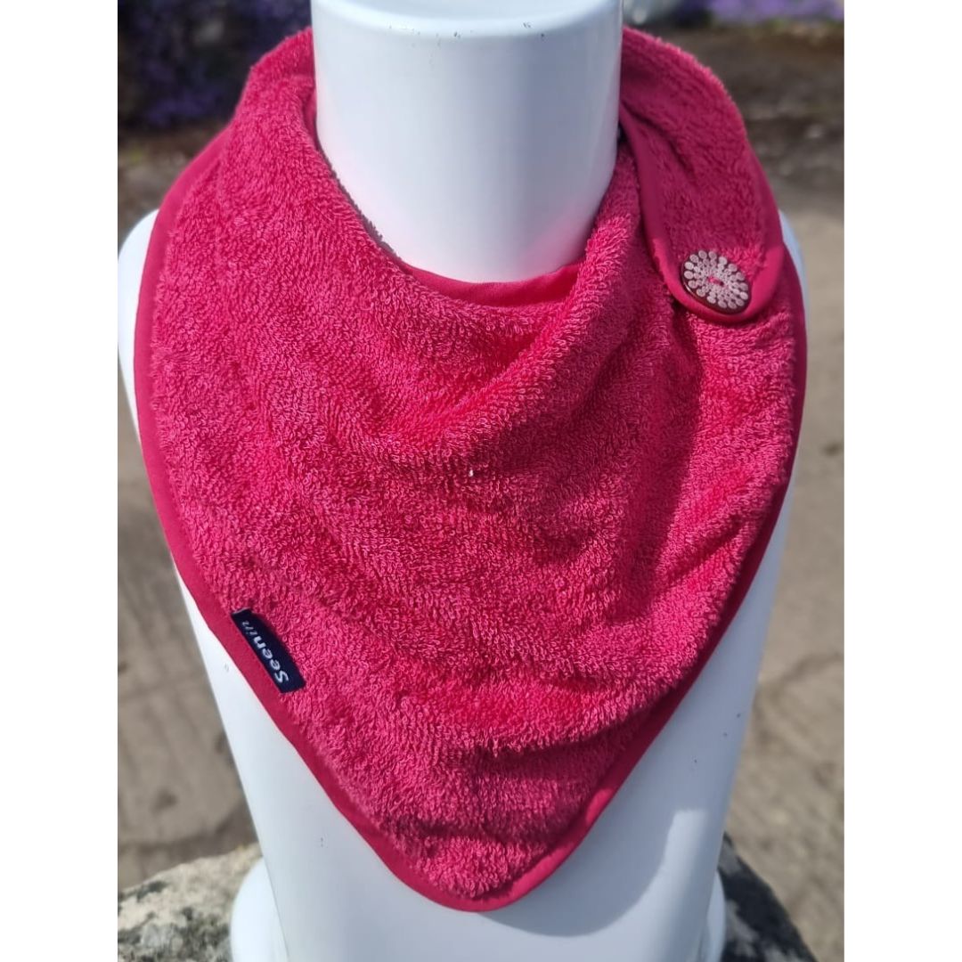 A bright pink textured bandana bib neck warmer with a small decorative floral button and a black brand tag reading 'HUNTS', displayed on a white mannequin torso.
