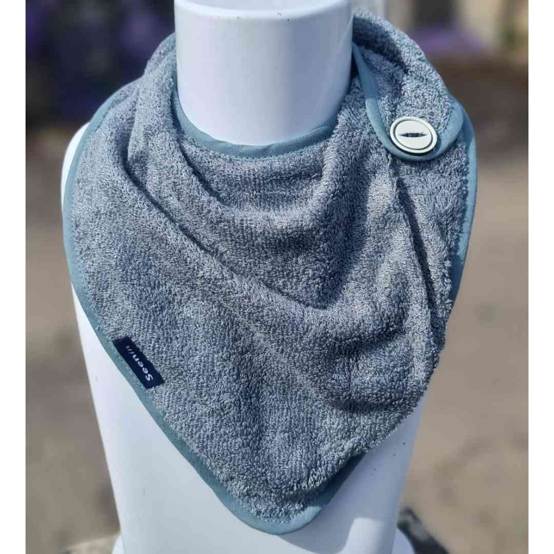 A light blue-gray terry cloth dog bandana bib with a snap button closure, displayed on a white mannequin torso.
