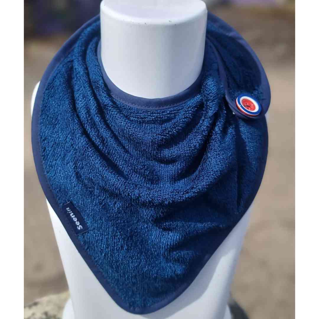 A dark blue textured bandana bib neck warmer with a small circular logo patch and a black brand tag, displayed on a white mannequin torso.