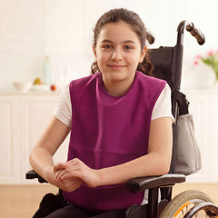 Young girl in a wheelchair wearing a purple vest, smiling indoors.