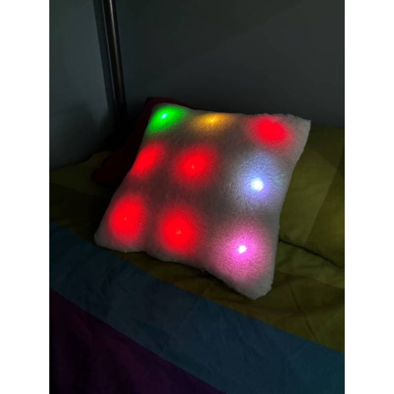 Light-up pillow with colorful LED lights on a bed in a dark room