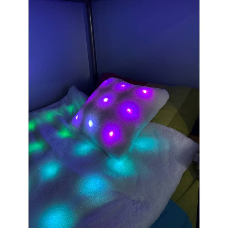 Glowing LED blanket and pillow on a bed in a dark room